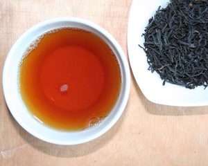 DE-ÖKO-006 Unregelmäßig lange schwarze Blätter, milder, weicher samtiger und nussiger Duft und Geschmack. Besonderheit – idealer Tee für den Abend – sehr magenfreundlich. Der Koffeingehalt ist verhältnismäßig gering, die Gerbstoffe sorgen für eine hervorragende Magenverträglichkeit. Der Tee ist sehr geschmackvoll und entfaltet sich in jedem Wasser bestens. Zubereitung: 1 geh. TL/Tasse,10g/l, kochendes Wasser Ziehzeit: ca. 4 Minuten Zusätze: Zucker oder Honig Ursprung: China VR Kommentar der Fachpresse: Farbe : dunkles Bernstein nahe an Mahagoni Duft : reich, mächtig nach Malz, Honig, Schokolade nebst erfrischendem Hauch von Citrus. Auch ein sanfter Rauchton ist erkennbar. Geschmack : mild lange anhaltend, geprägt von honigmalzigen Noten Besonderes Merkmal ->die geschmeidige Fülle, die Vielschichtigkeit Empfehlung : wie naturgeboren zu Aufläufen jeder Art, Zu Quiches, Cremesuppen, dunklen Ragouts, Käse, Gulasch sowie Abendbrot-Platten Zubereitung : ca. 7 gehäufte Teelöffel in einem Liter heißem Wasser zwei bis drei Minuten ziehen lassen – je nachdem, wie kräftig man den Tee haben will.